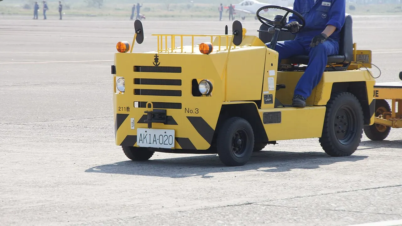 A yellow aircraft towing tractor parked on an airfield apron
