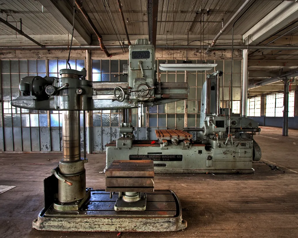A large radial arm drill press on the wooden floor of an old machine shop