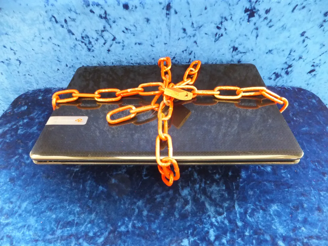 A closed laptop wrapped in an orange chain and padlock