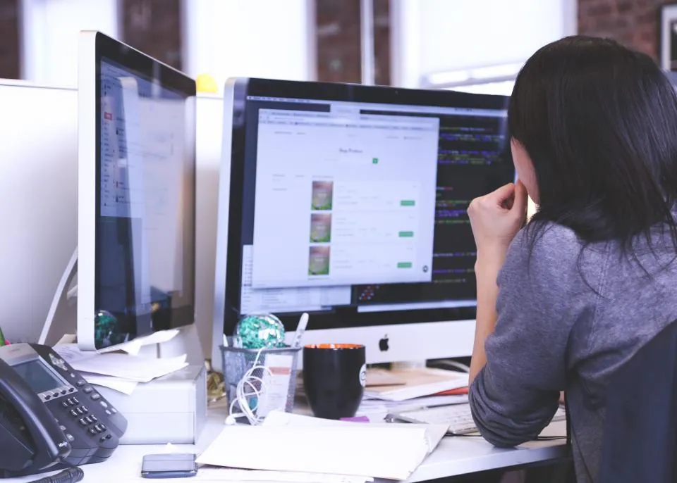 A person working at a desk with two monitors and an office phone